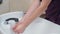 Stylist in dark red uniform washing her hands in white washstand, close shot. Hairstylist washing hands befor shaving