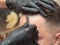 Stylist shaving clients forehead with open razor in barbershop, close up view. Hands in black rubber gloves with open