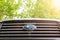 Subaru emblem on a radiator grill against green foliage and with sunlight to the right