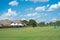 Suburban park with grassy lawn, tall post lights and people walking near residential house backyard white high spike outdoor