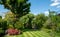 Suburban, well stocked garden in London UK, with neatly mown striped lawn, tall oak tree, colourful azalias and other trees.