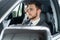 Success in motion. Handsome young man in full suit smiling while driving a car.