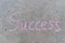 Success written with pink sidewalk chalk on gray concrete background