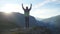 Success young man raising his hands high on top of the big mountain at beautiful golden sunset