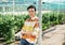 Successful Asian female horticulturist posing in large greenhouse