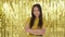 Successful beautiful Asian girl smiles broadly against a gold background and crosses her arms strenuously. Chic festive