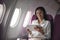 Successful beautiful young asian business woman sits in airplane cabin plane and works on digital tablet with stylus