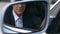 Successful businessman sitting in car and looking in side view mirror, driver