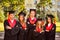 Successful confident five graduates in robes and hats standing in row while crossing hands