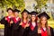 Successful confident five graduates in robes and hats with tassel showing thumbs up