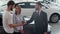 Successful deal between car salesman and young couple in car dealership.