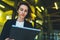 Successful female banker using tablet and wireless earphones outdoors near office background yellow neon lights