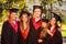 Successful joyful five graduates in robes and hats smiling and hugging