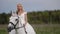 A successful lady riding a white posh horse gallops across a field in a white dress