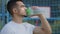Successful middle eastern indian man athlete latino runner holding drinking from sport bottle during workout pause at