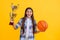 successful proud teen basketball girl with champion cup award. teen basketball girl hold award cup isolated on yellow