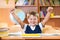 Successful schoolboy with hands up sitting at desk