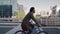 Successful smiling professional young man riding bicycle in front of modern buildings at background