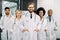 Successful team of multiracial male and female medical doctors in white coats, looking at camera and smiling while