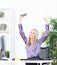 Successful young blonde businesswoman, victory gesture, hands up, smiling at office