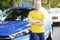 Successfull happy young man and his car in soft sunset light on urbanistic background. Busines man with vehicle on roadside.