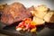 Succulent thick juicy portions of grilled fillet steak served with roasted potatoes and peppers on black granite board