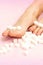 Sugar cubes lying in a row on female feet on pink background with copy space, depilation concept.
