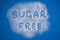 Sugar Free words hand written on a heap of white sugar on a blue background top view. Stop diabetes and excessive sugar intake con