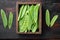 Sugar snap peas, raw ripe baby pods, in wooden box, on old dark  wooden table background, top view flat lay