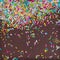Sugar sprinkle dots, decoration for cake and bakery, as a background. On chocolate broun background,