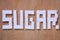 SUGAR word lined with refined sugar cubes on wooden brown background