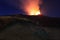 Suggestiva eruzione del vulcano Etna con esplosione di lava dalla cima del cratere con sfondo il cielo stellato e paesaggio