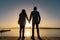 Suggestive silhouette back shot of young couple in love holding hands standing on a pier watching the sun setting or rising in