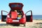 Suitcase and beach accessories in car trunk on sand near sea