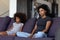 Sulky african child and mother sitting on sofa not talking