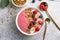 Summer acai smoothie bowls with raspberries, banana, blueberries, and granola on gray concrete background. Breakfast bowl with