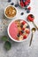 Summer acai smoothie bowls with raspberries, banana, blueberries, and granola on gray concrete background. Breakfast bowl with