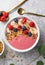 Summer acai smoothie bowls with raspberries, banana, blueberries, and granola on gray concrete background. Breakfast bowl with