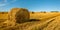 summer agricultural landscape. A straw bale left in the foreground on field after harvesting under a beautiful blue sky