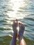 Summer background. Female legs in sea against background of reflection of sunlight in water