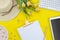Summer background flat lay of yellow tulips with tablet keyboard and clipboard, copy space for text. Flyer mockup