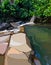 Summer background with a pond with stone shores in green bushes