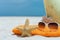 Summer beach bag with towel, sunglasses and coral on sandy beach