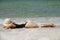 Summer beach vacation. Woman in black swimwear lying on sandbeach. Girl enjoying sunbath near sea. Sexy tanned lady in