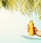 Summer beverages background with tropical palm leaves and yellow drink bottle in female hand at pastel blue background