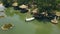 Summer bungalows with thatched roof and boat in green lake in water villa resort drone view. People swimming in green