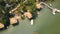 Summer bungalows with thatched roof and boat pier on shore green lake in luxury mountain hotel aerial view. Cottages on