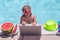 Summer business. Child remote working on laptop in pool. Little business man working online on laptop in summer swimming