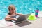 Summer business. Child remote working on laptop in pool. Little business man working online on laptop in summer swimming