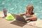 Summer business. Child remote working on laptop in pool. Little business man working online on laptop in summer swimming